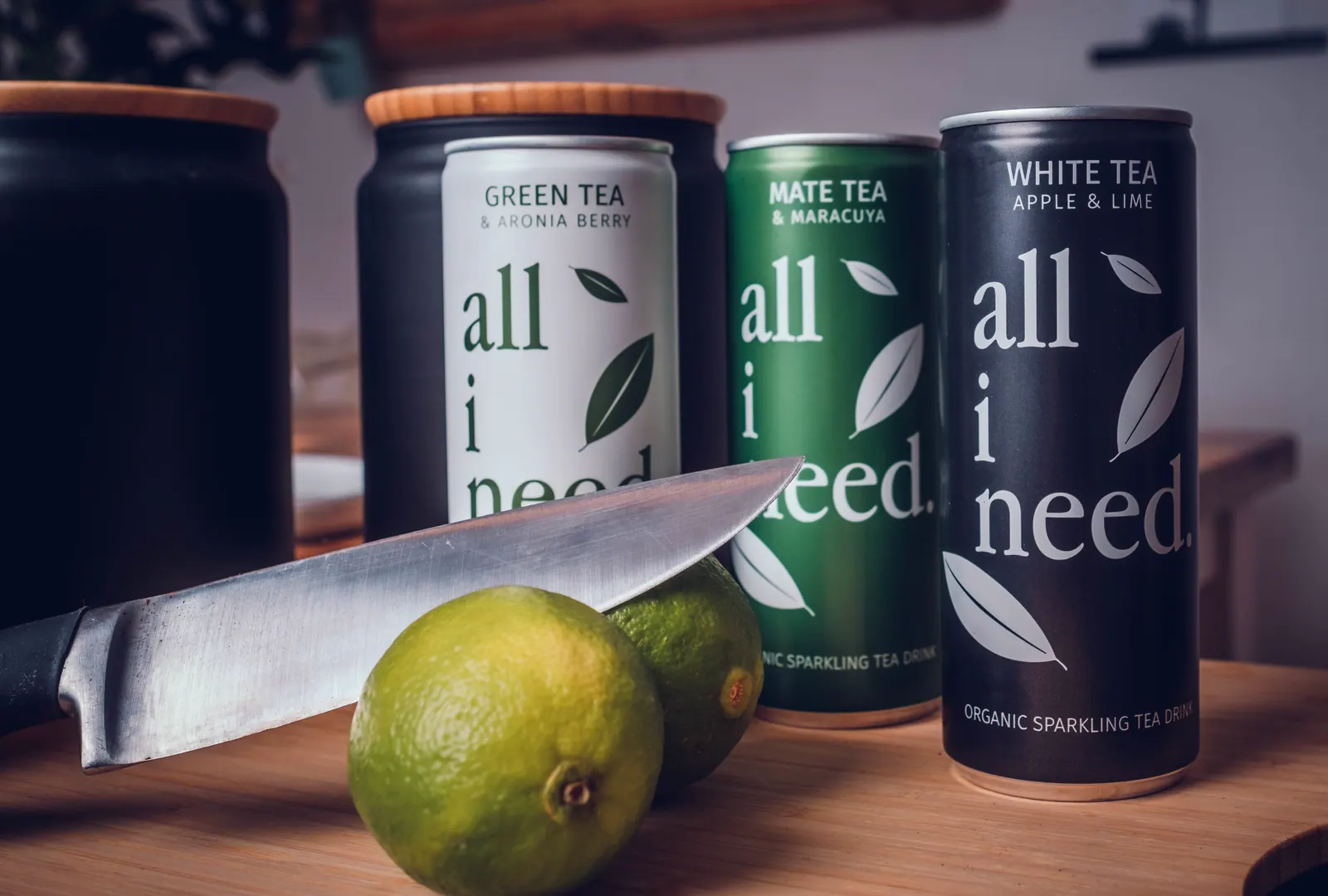 Drei Getränkedosen der Marke all i need neben Limette und Messer